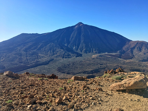 A rugged, almost plant-free mountainous landscape dominated by the conical silhouette of a volcano